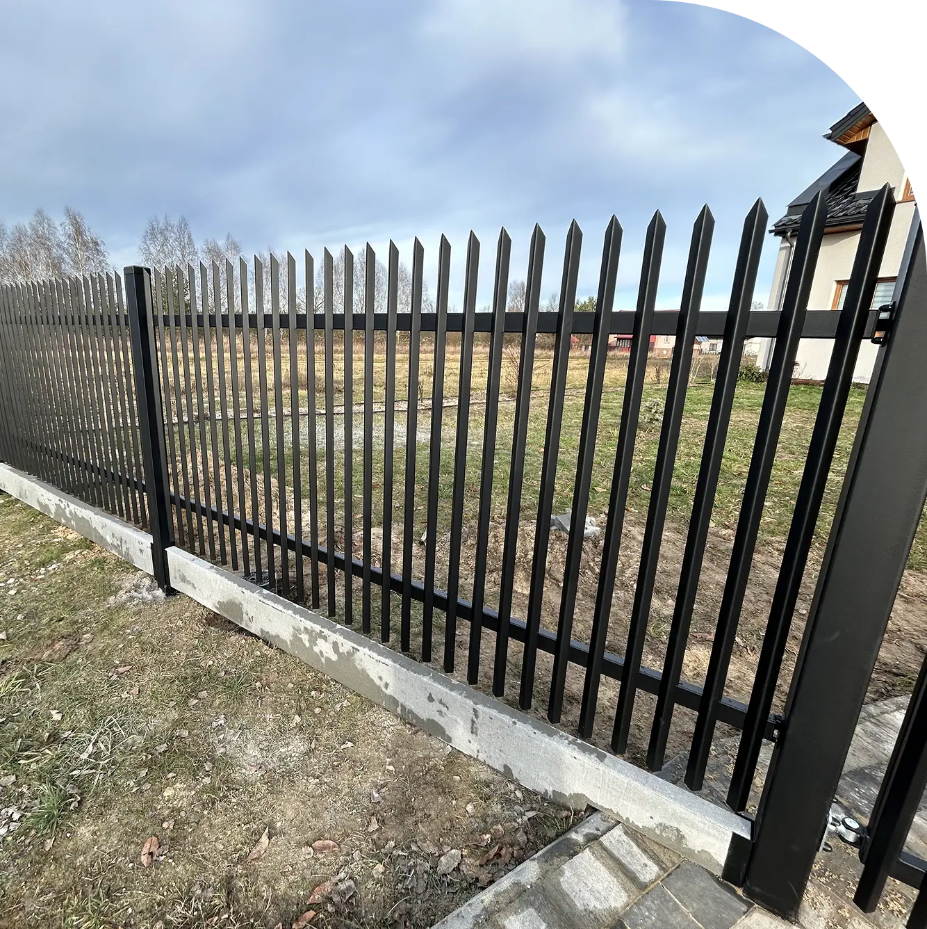 Ogrodzenia palisadowe w czarnym kolorze zamontowane na betonowej podmurówce na tle trawnika