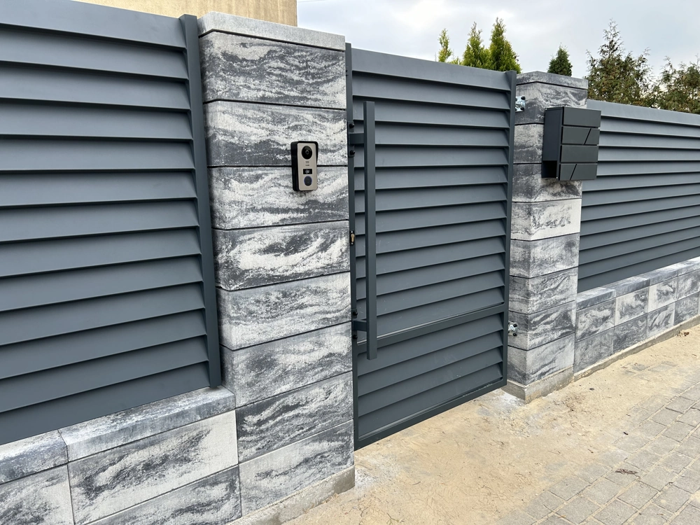 Ogrodzenie żaluzjowe z furtką, słupkami z bloczków oraz domofonem w szaro-niebieskim kolorze