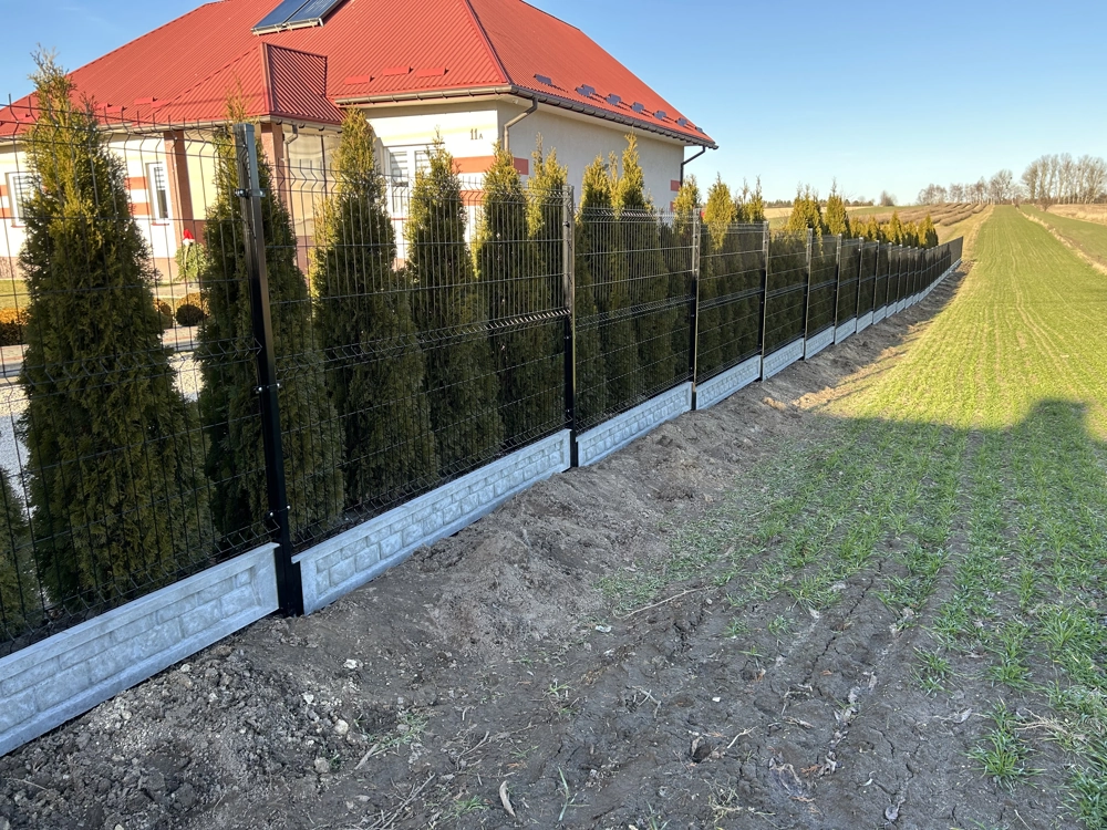 Ogrodzenia panelowe z czarną siatką i kamienną podmurówką z nasadzonym żywopłotem