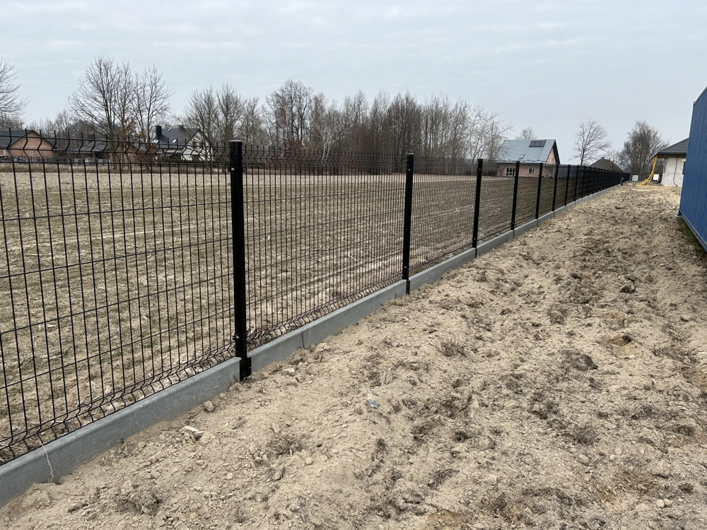 Czarne ogrodzenie panelowe montowane na betonowej podmurówce w otwartym terenie