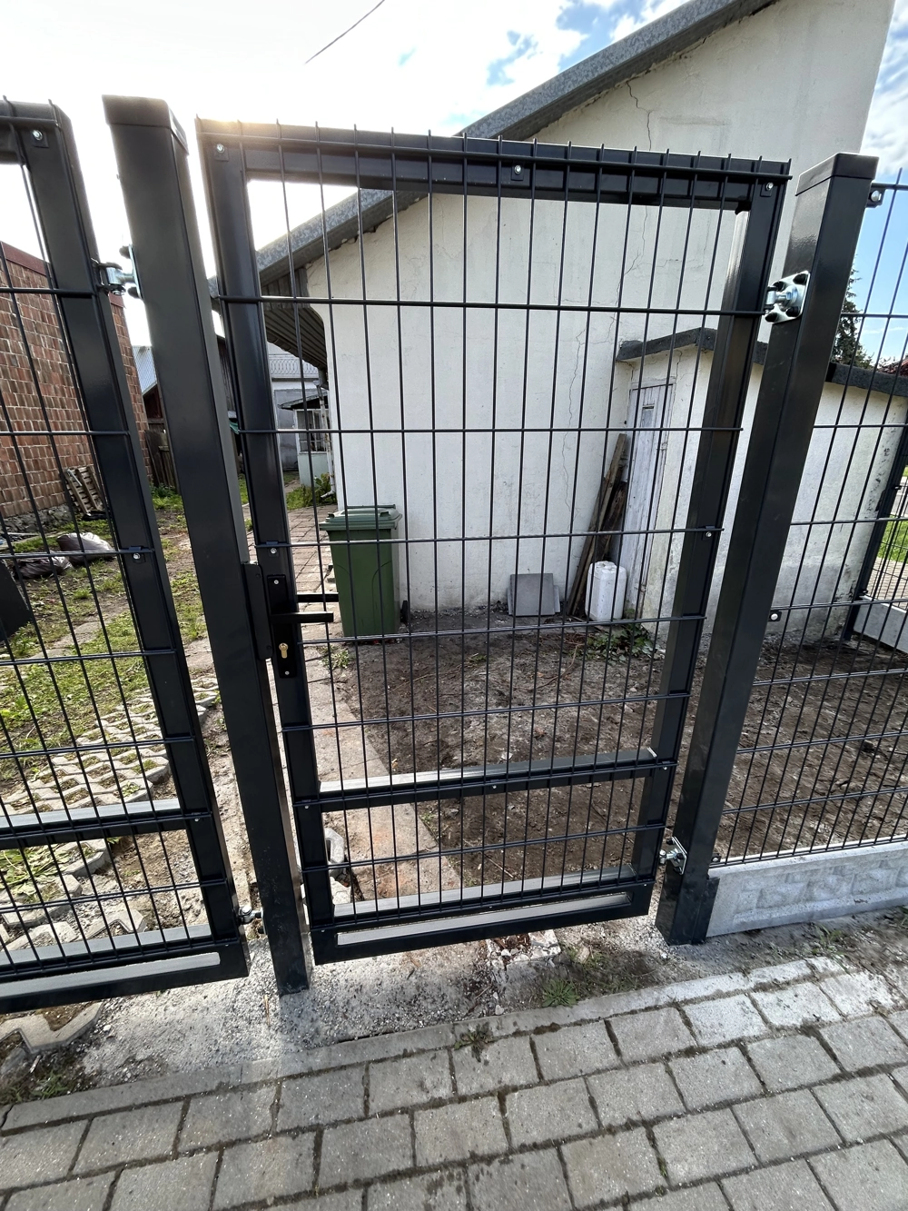 Czarna furtka panelowa z metalowymi przęsłami zamontowana w ogrodzeniu