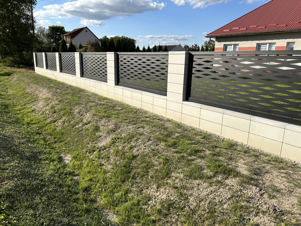 Szare panele ogrodzenia wycinane laserowo na jasnej murowanej podmurówce przed domem