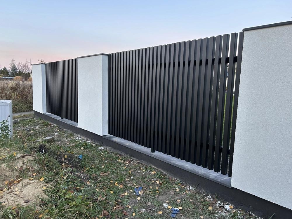 Ogrodzenie żaluzjowe z czarnych aluminiowych lameli osadzone na białych słupkach murowanych