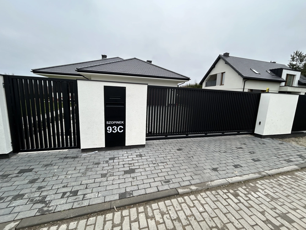 Ogrodzenie żaluzjowe w odcieniu czarnym z bramą wjazdową i furtką na tle nowoczesnego domu