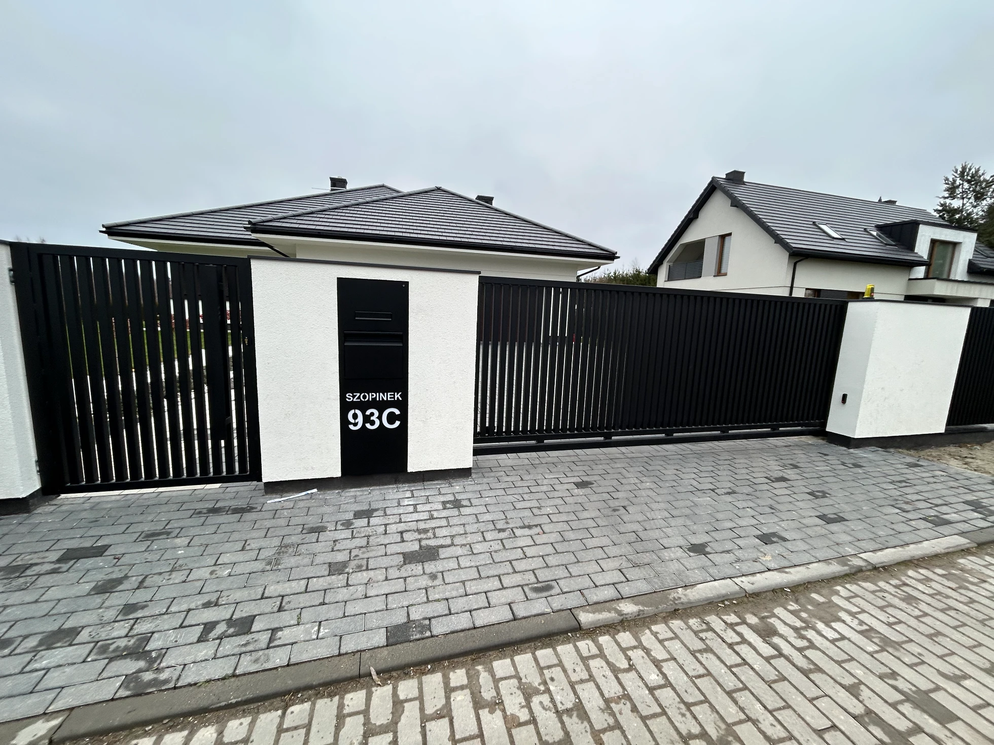 Ogrodzenie żaluzjowe z czarną bramą wjazdową i furtką przed nowoczesnym domem